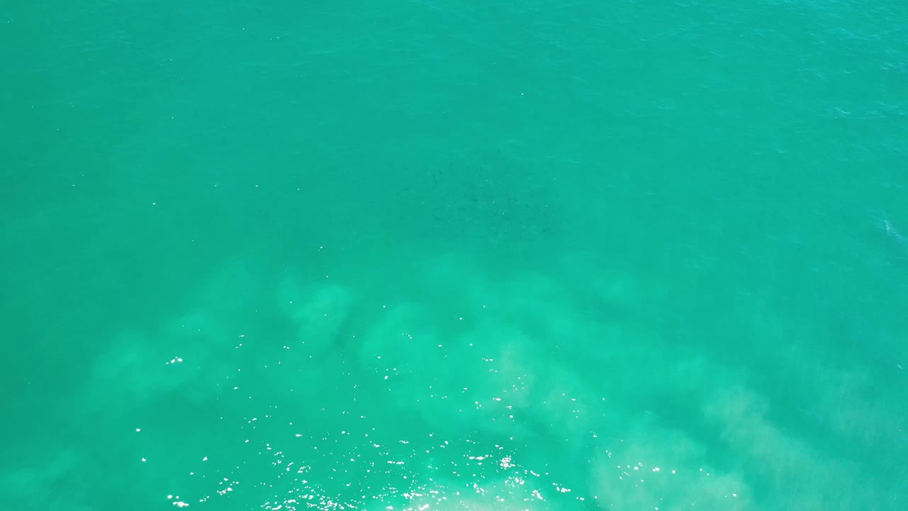 Turquoise ocean surface in Los Cabos, Mexico, with brighter specks of reflected sunlight clustered near the lower left and no visible people.