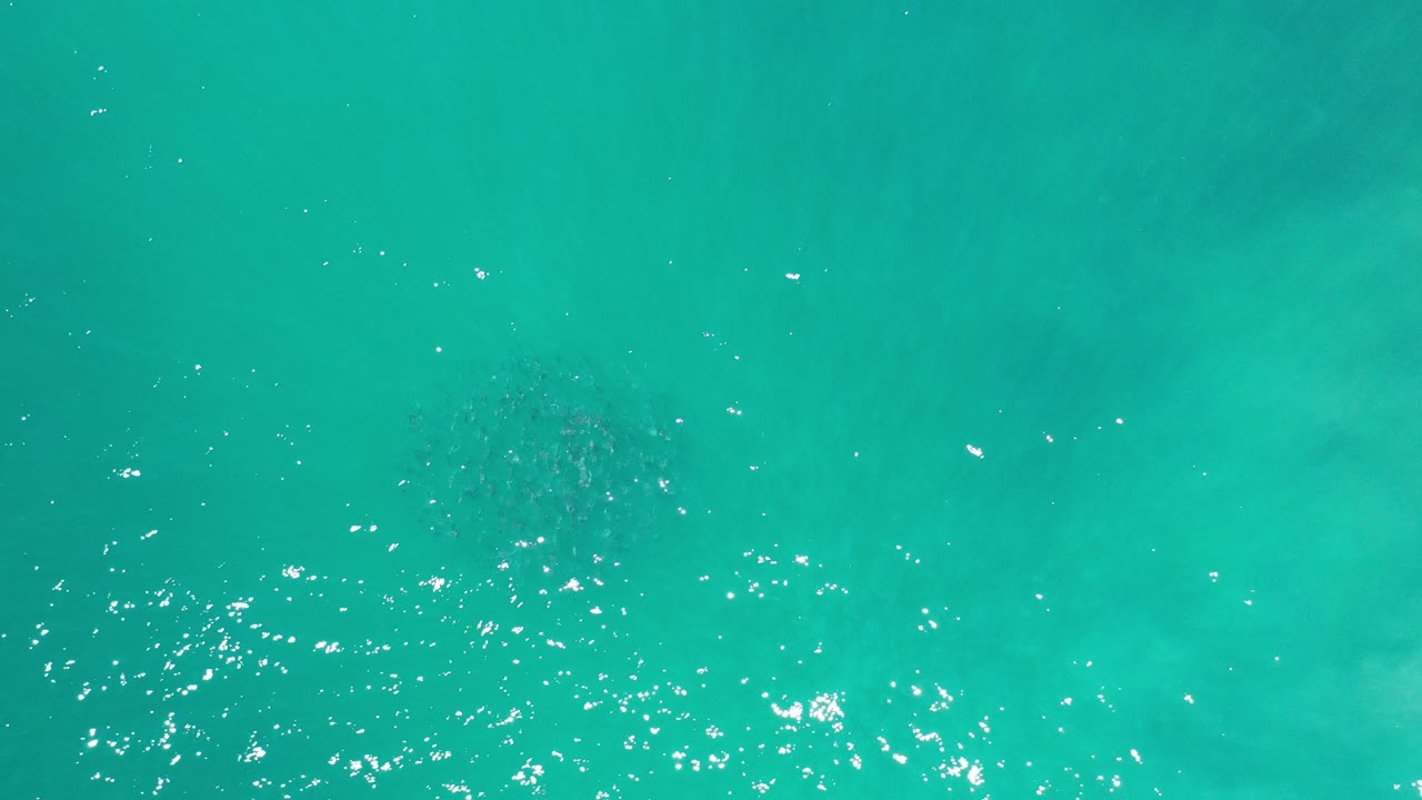 Overhead view of turquoise ocean water in Los Cabos, Mexico, with scattered sun flecks near the lower left and no visible people.