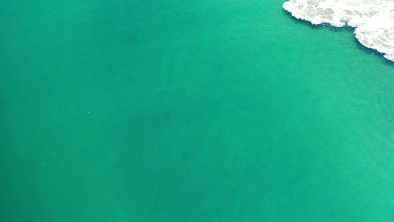 Bright turquoise sea with a small strip of surf in the upper right corner.