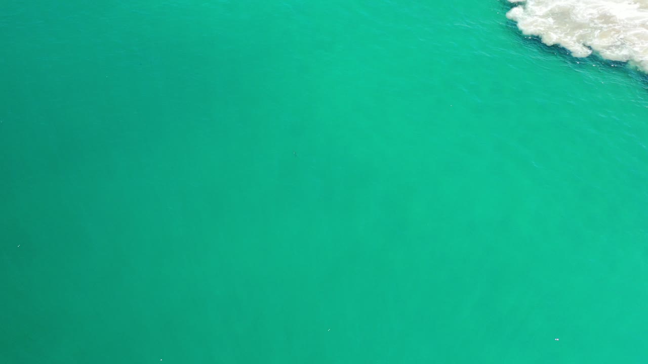Overhead view of green sea in Los Cabos, Mexico, with a small patch of white surf at the upper right and no visible people.