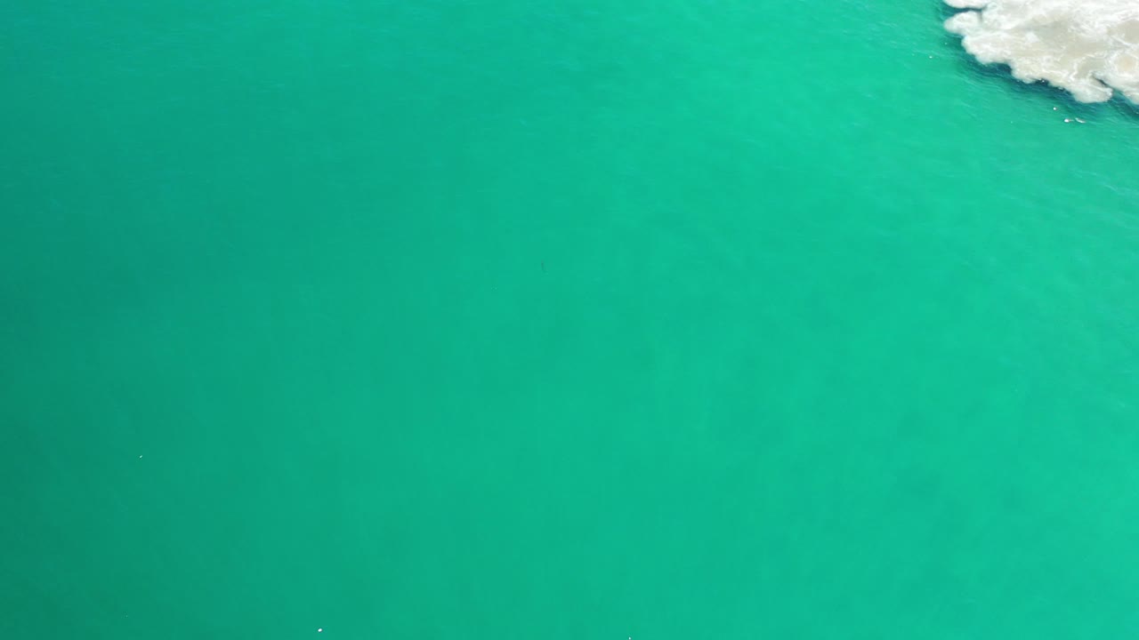 Green sea fills the overhead frame while a brighter surf patch sits along the upper right edge, with no people or boats visible.