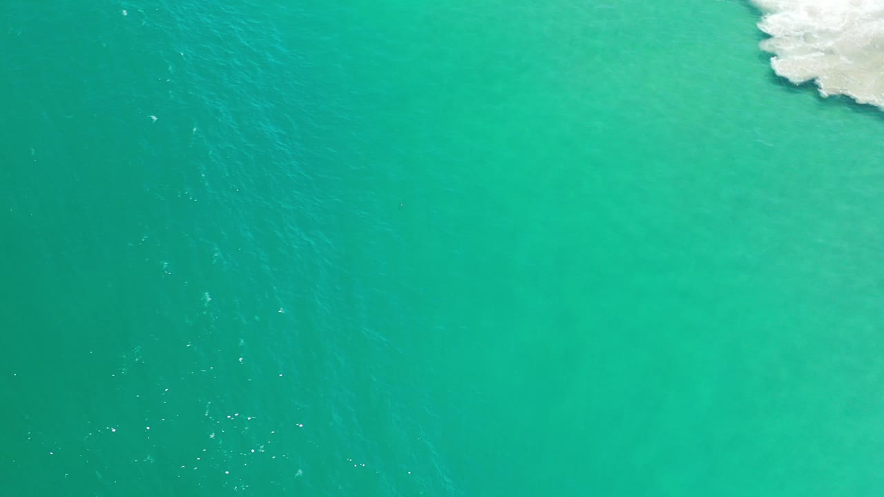 Bright turquoise water with a narrow area of surf foam in the upper right corner.