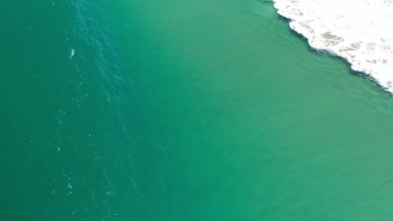 Overhead view of green ocean water in Los Cabos, Mexico, with white surf breaking along the upper right edge and no visible people.