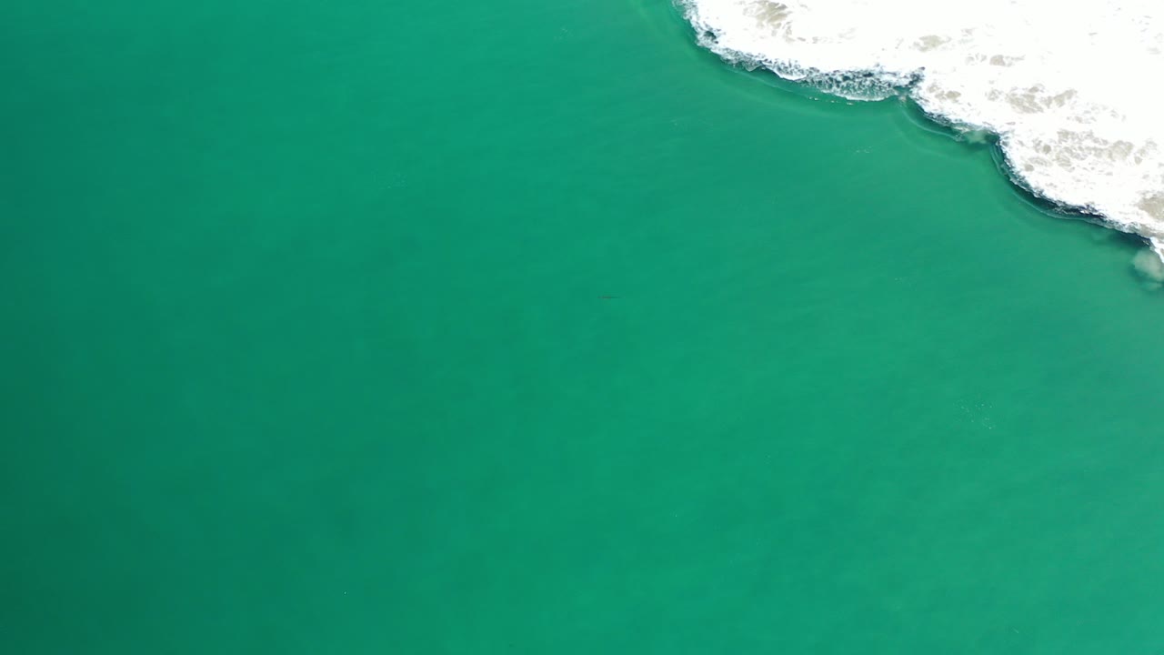 Overhead view of blue-green water in Los Cabos, Mexico, with a band of white surf along the upper right edge and no visible people.