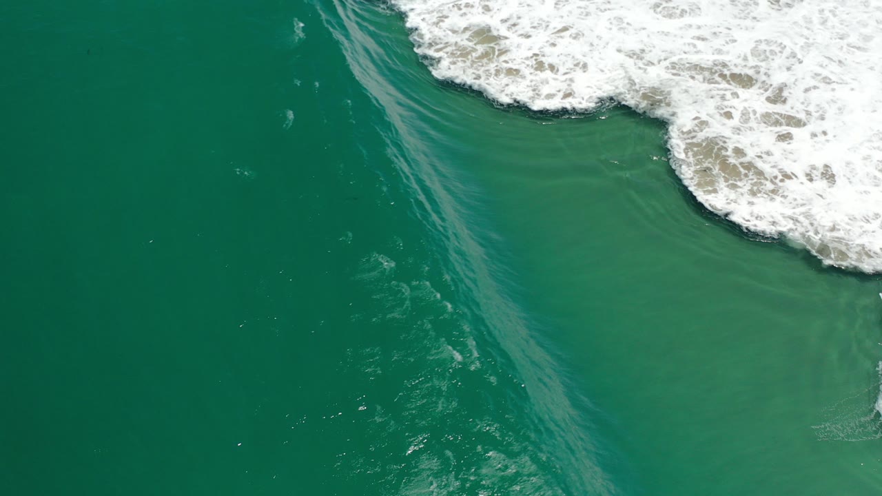 Overhead view of blue-green ocean water in Los Cabos, Mexico, with white surf curling across the upper right edge and no visible people.