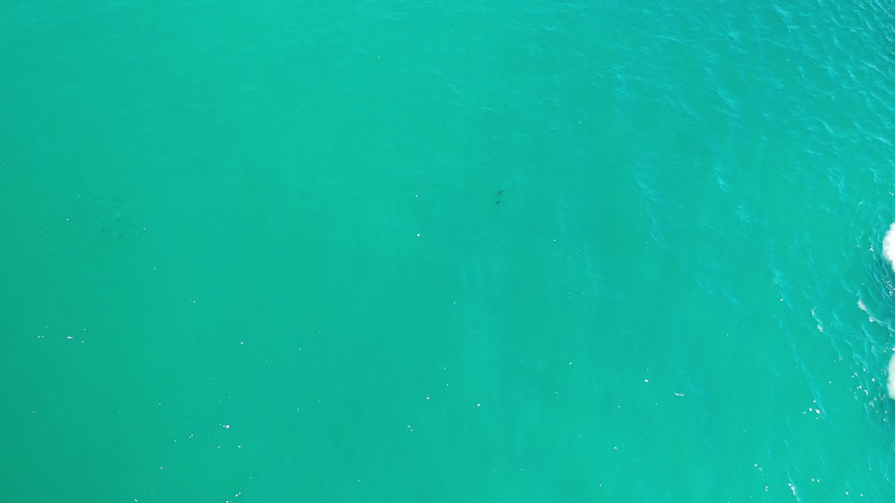 Turquoise water with faint wave streaks and foam at the far right edge.