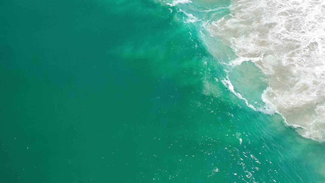 Open teal ocean with a patch of breaking surf at the upper right.