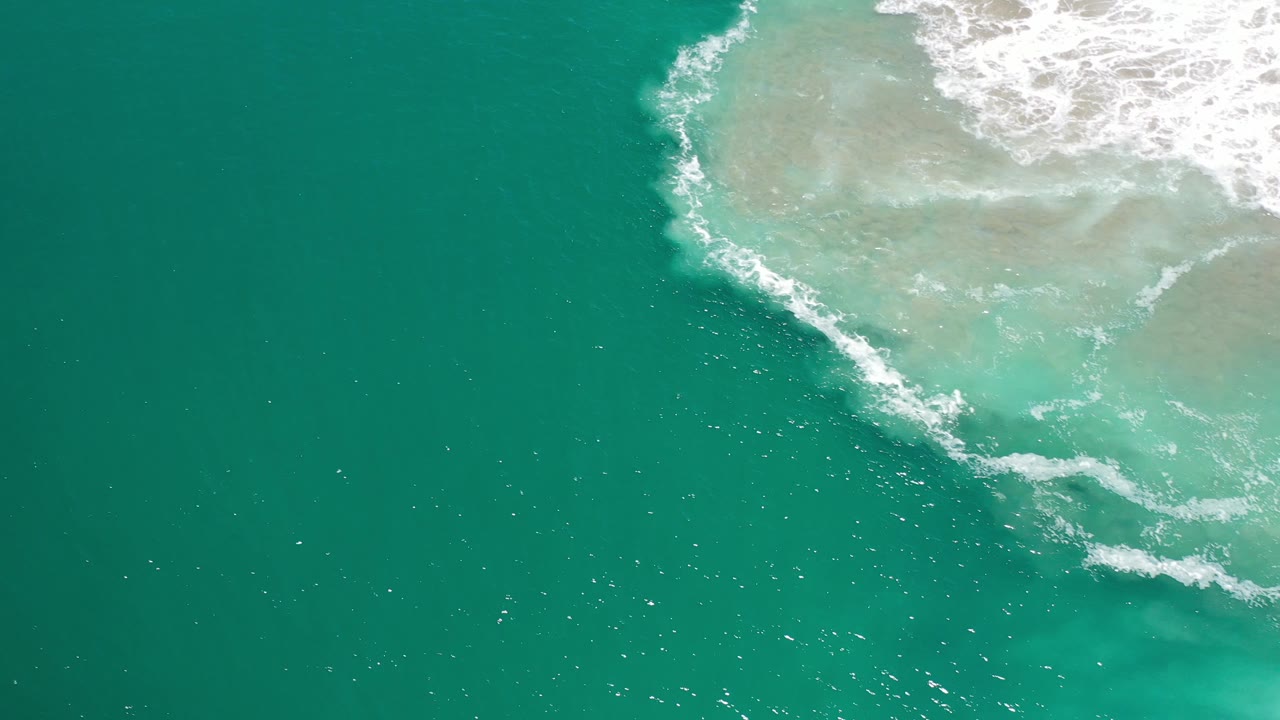 Open green-blue ocean with white foam and shallow sand at the top right.