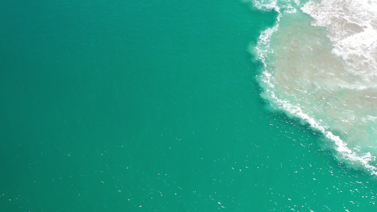 Overhead teal ocean with white surf entering from the upper right.