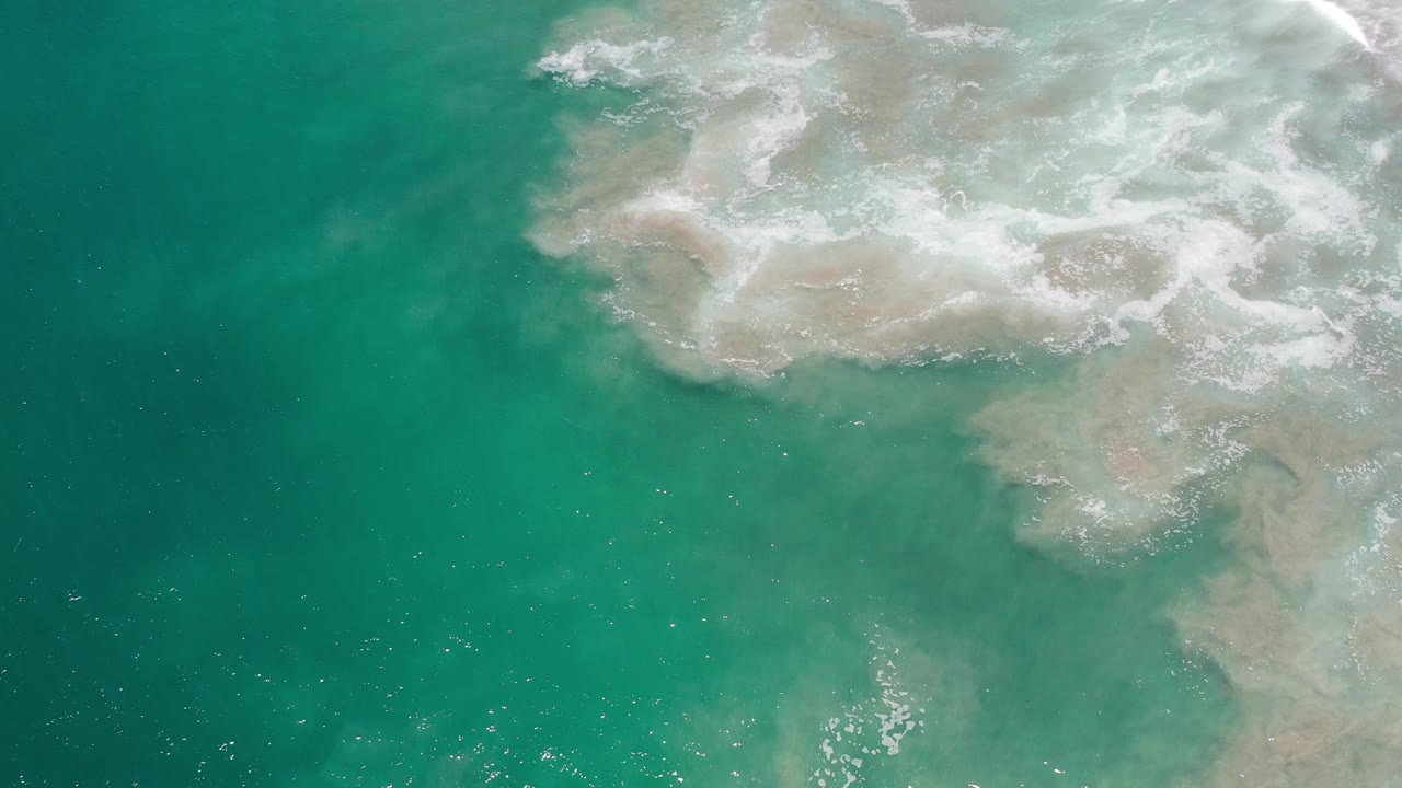 Green ocean water with white foam and sandy turbulence