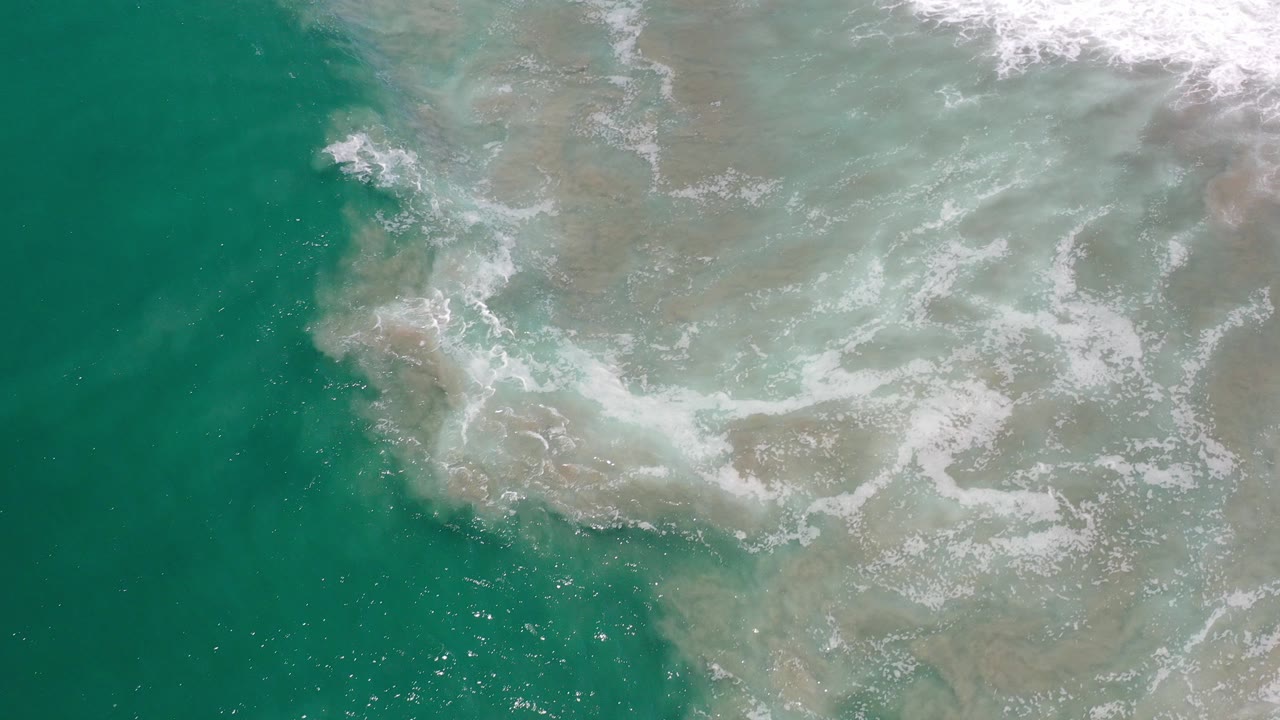 Overhead blue-green surf and sandy shallows with white foam.