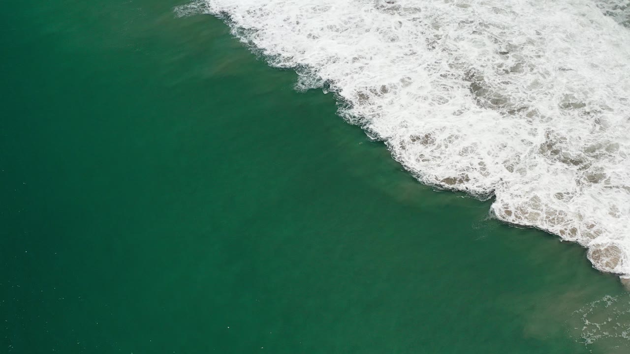 Green ocean water with white foam entering from the upper right.