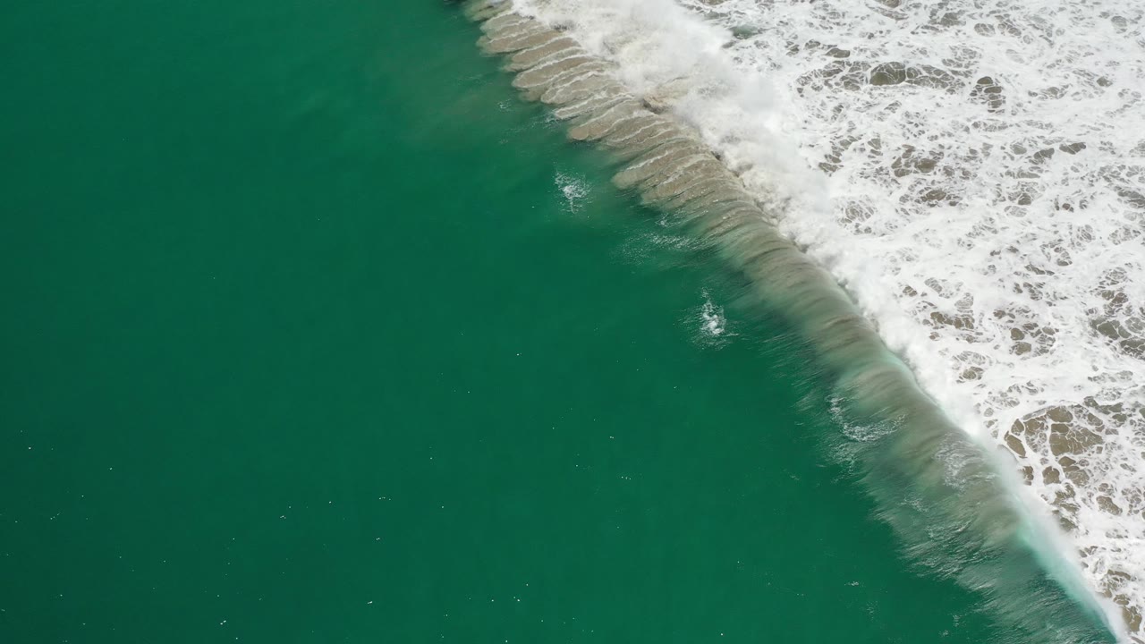 White wave foam rolling along the top edge of green ocean