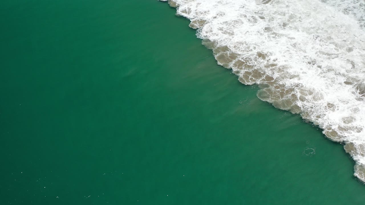 Overhead view of green Pacific water at Los Cabos, Mexico, with white breaking surf along the upper right edge and no visible people.