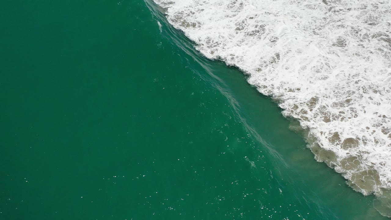 Overhead view of teal water in Los Cabos, Mexico, with white surf entering diagonally from the upper right and no visible people.