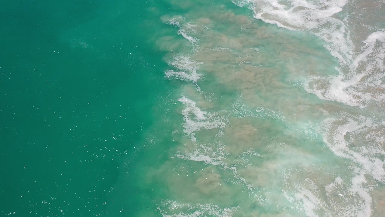 Top-down ocean surface with foamy surf entering from the upper right