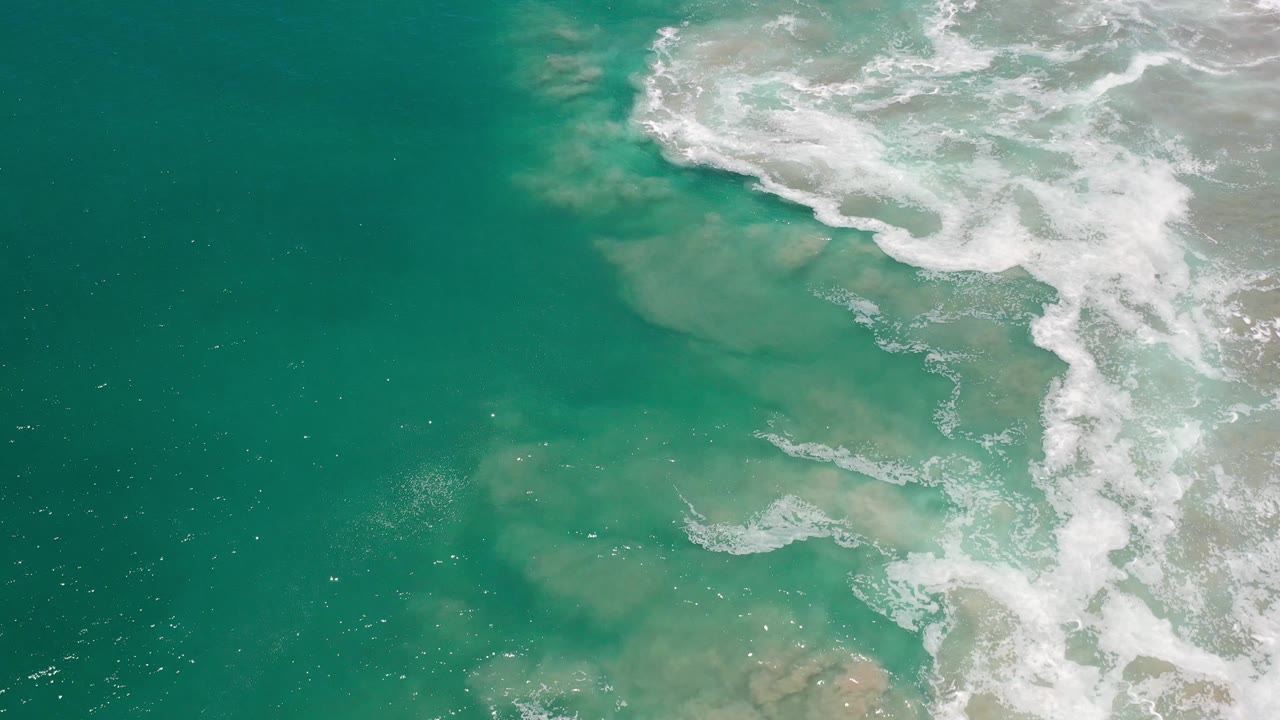 White surf band over teal water with sand patches beneath.