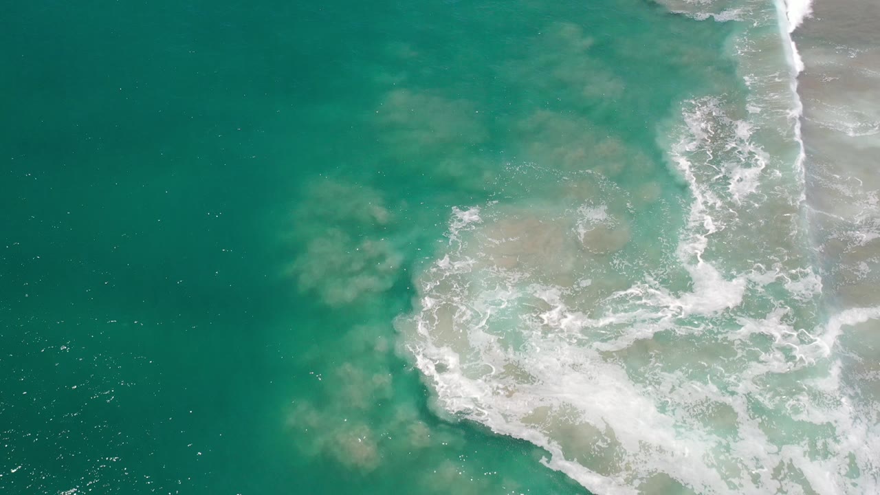 Top-down surf line with turquoise water and pale submerged sand.
