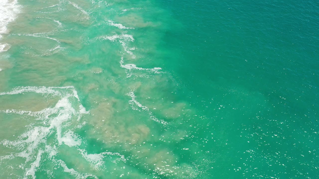Aerial view of clear ocean with white surf curling at the left edge.