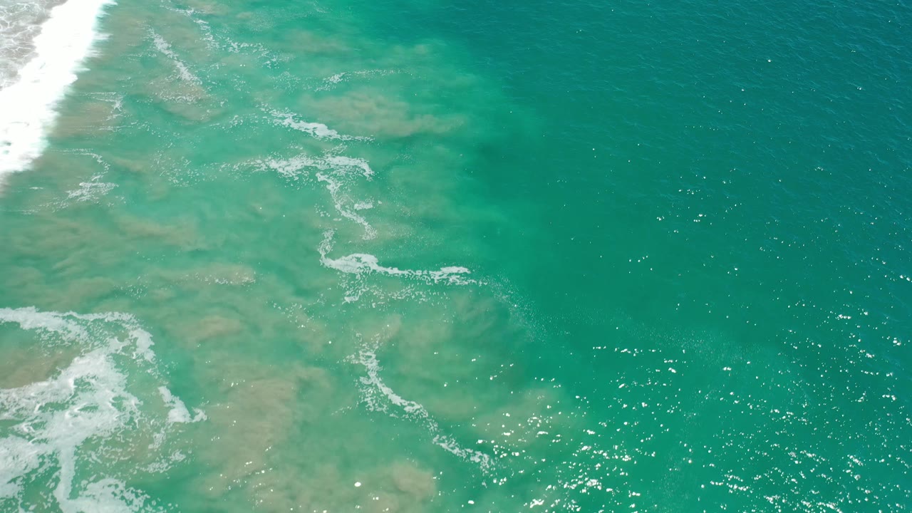 Sparkling turquoise water with broken white foam near the left side.