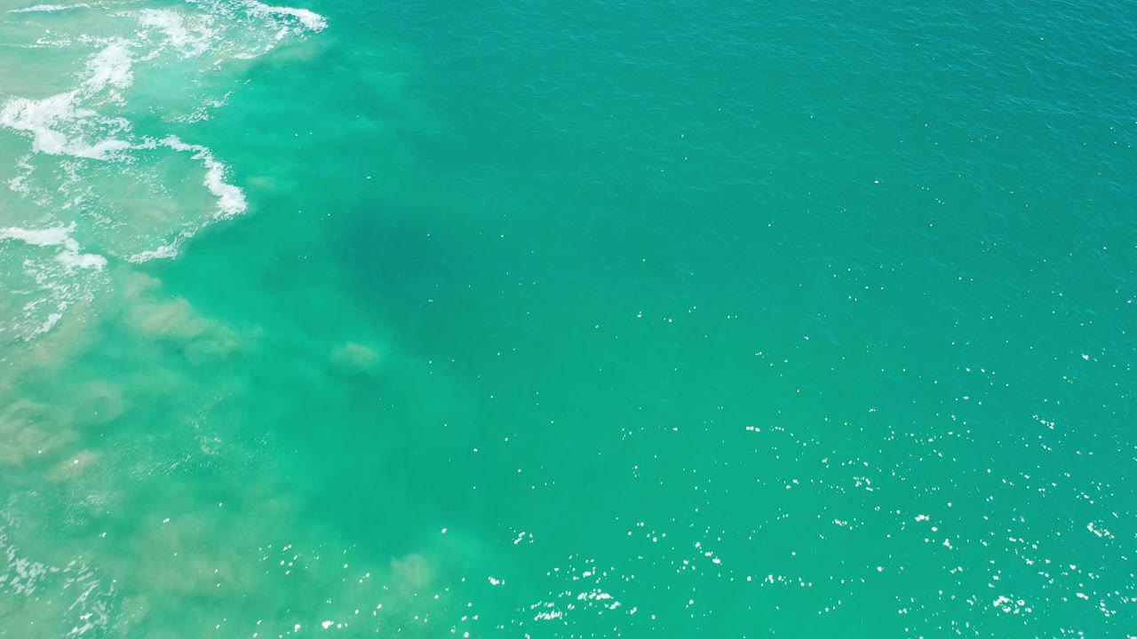 Aerial view over turquoise ocean water in Los Cabos, Mexico, with white surf entering at the upper left and no visible people.