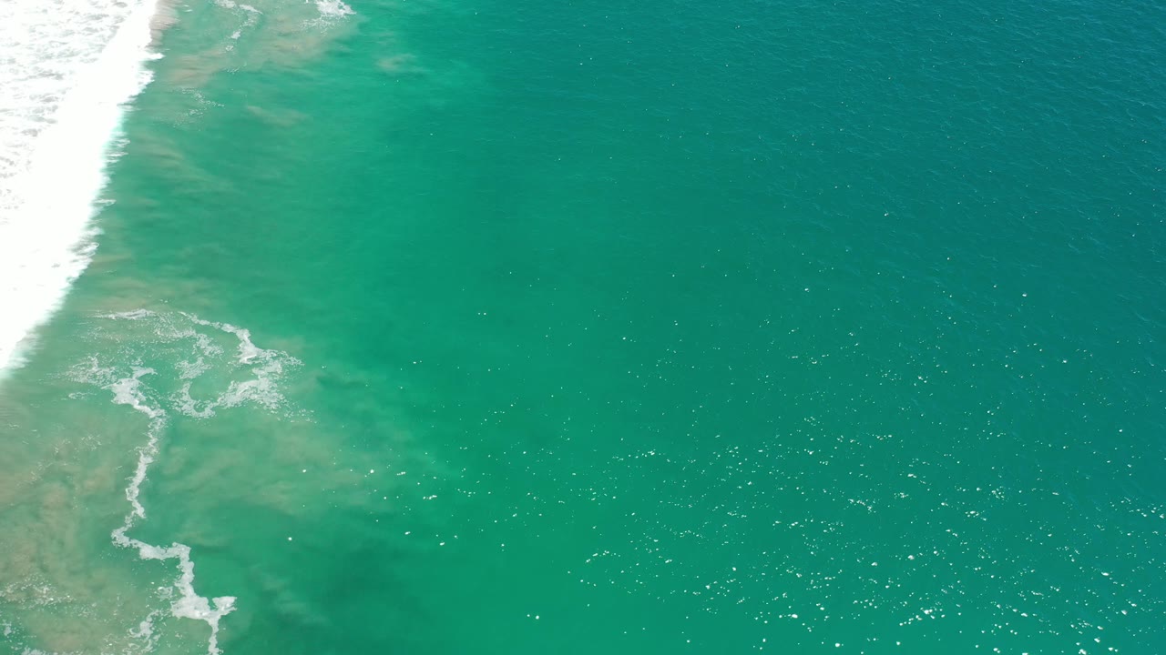 Turquoise-green water with surf foam at left and open sea to the right.