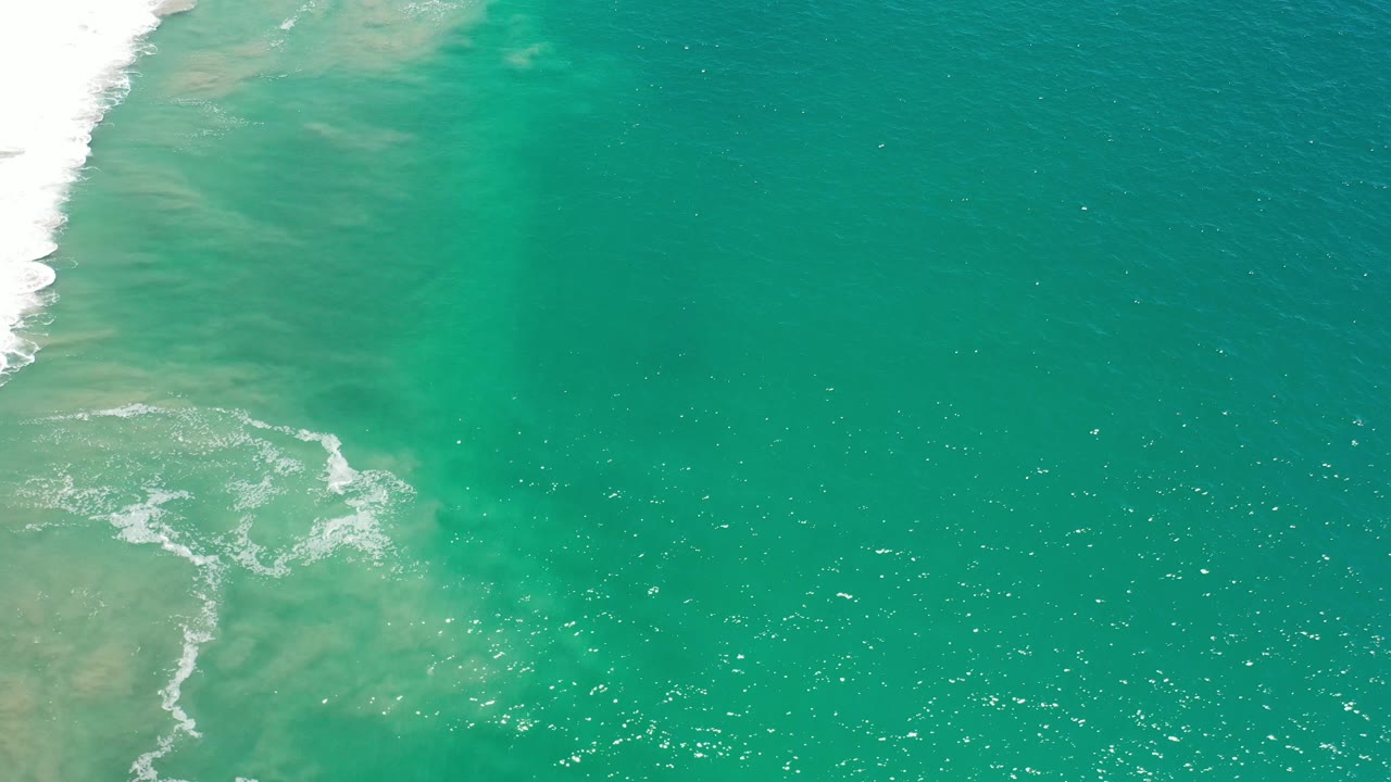 Overhead ocean view with surf foam, sandy water, and bright water reflections