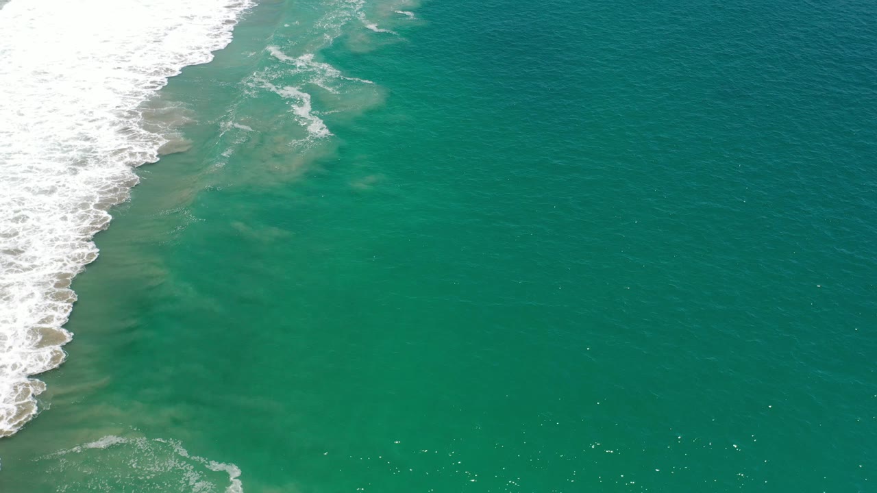 Open green ocean with surf foam along the upper left.