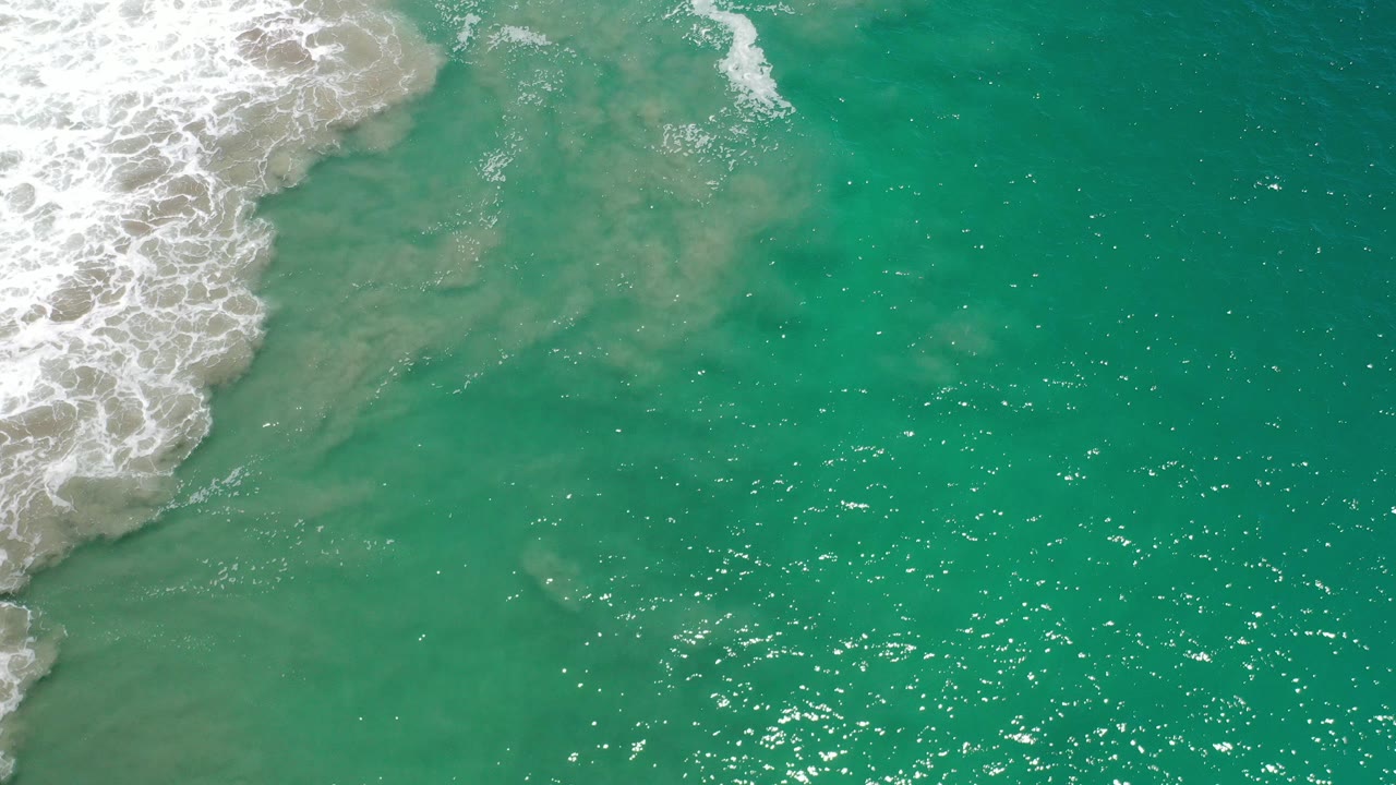 Overhead turquoise ocean with white surf entering from the upper left.
