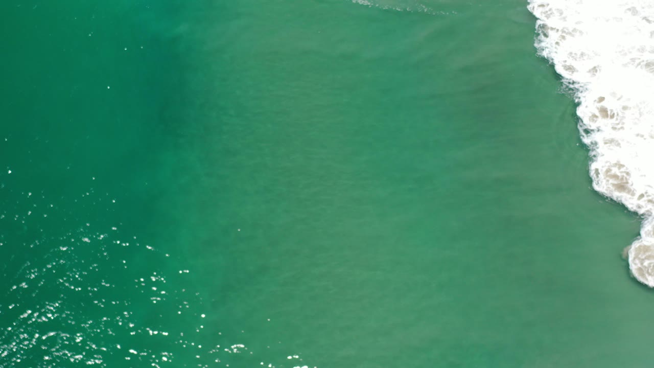 Overhead teal ocean water with white surf at the right edge.