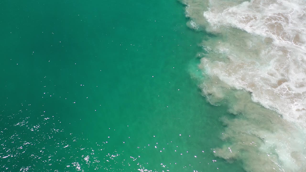 Open turquoise water with surf foam curling in from the upper right.