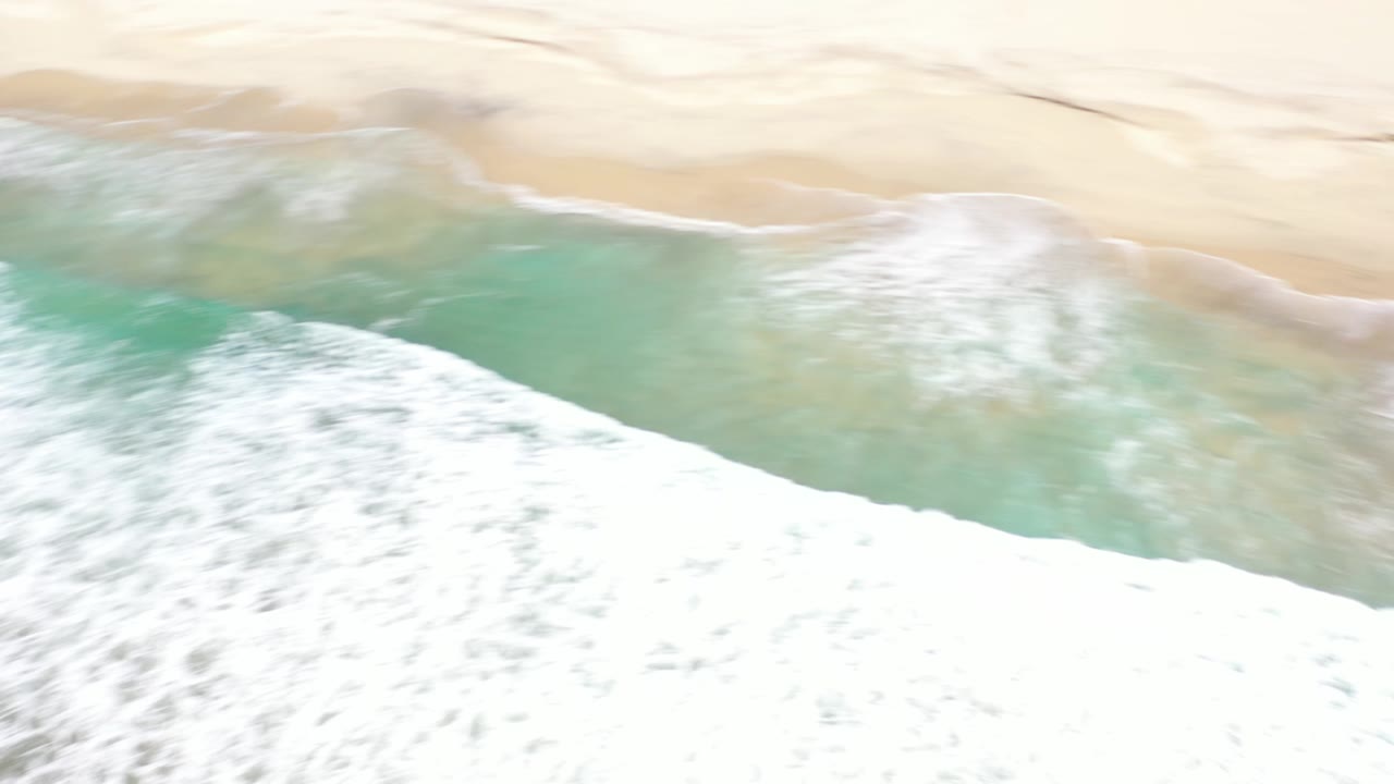 Turquoise water and white surf beside empty sand.