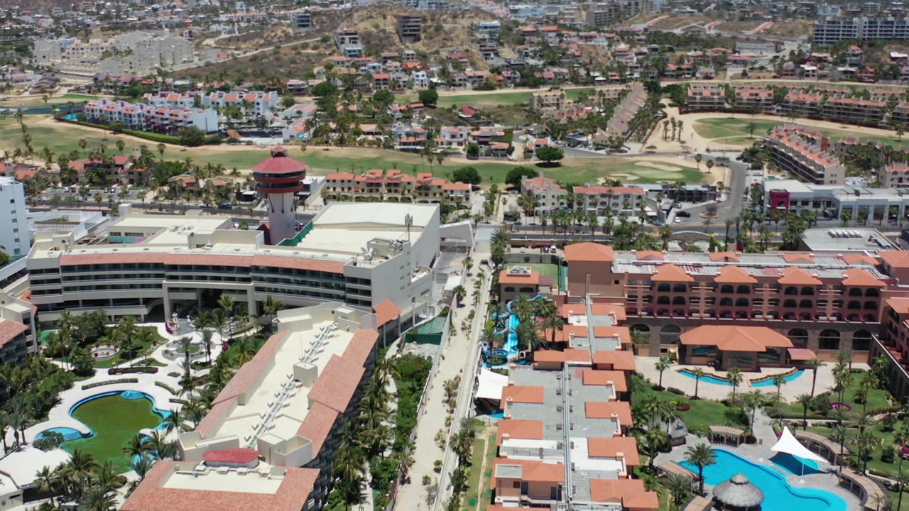 Aerial view over resort buildings, pools, roads, and hills.
