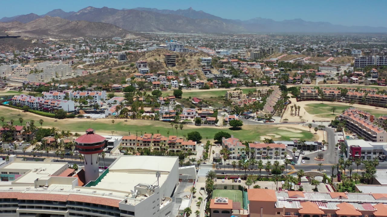 Wide aerial view over city roads, golf greens, buildings, and mountains