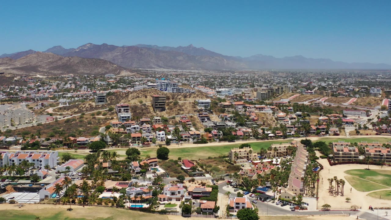 Aerial view of residential buildings, green grass, roads, and mountains.