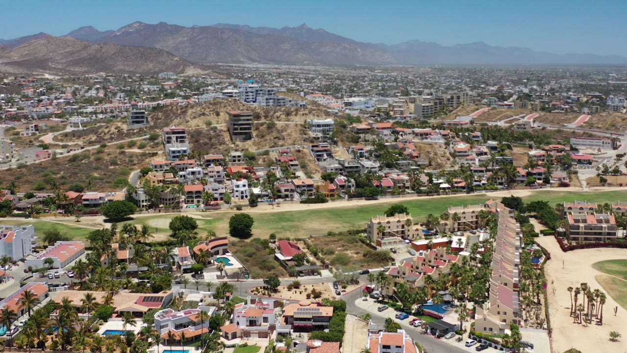 Aerial view of homes, lawns, dry hills, and mountains.