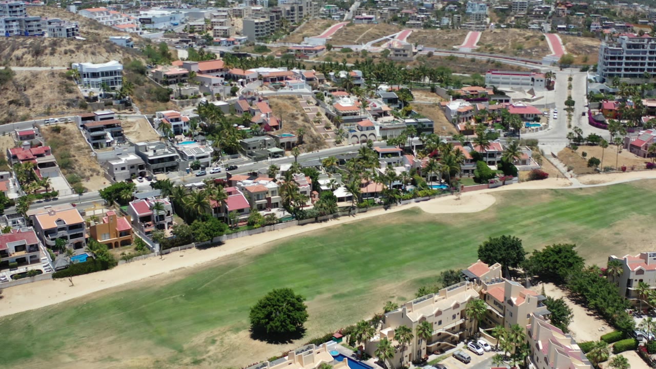 Drone-height view of villas beside a landscaped green and sandy path.