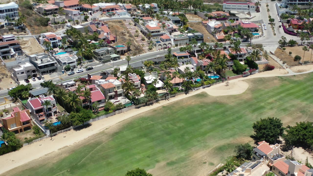 The Los Cabos aerial angle shows more of the road and clustered houses above a striped green lawn, with no visible people in the frame.
