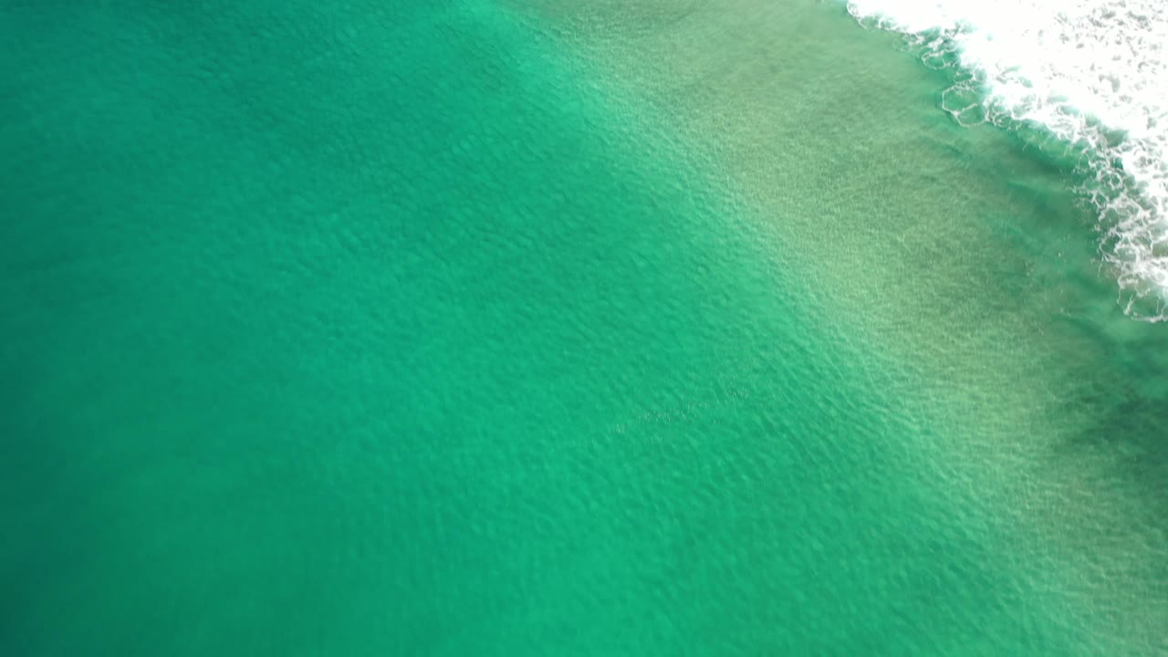 Turquoise-green water with surf foam along the upper right edge.