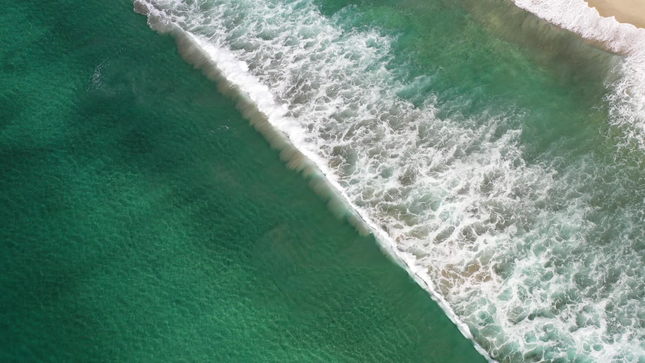 White surf line rolling across darker green ocean water.