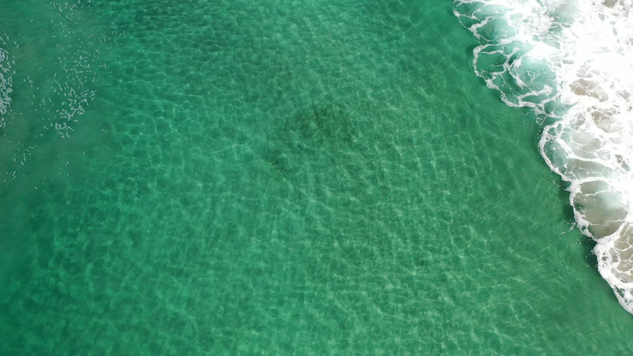 Turquoise-green ocean ripples with foamy shoreline at upper right