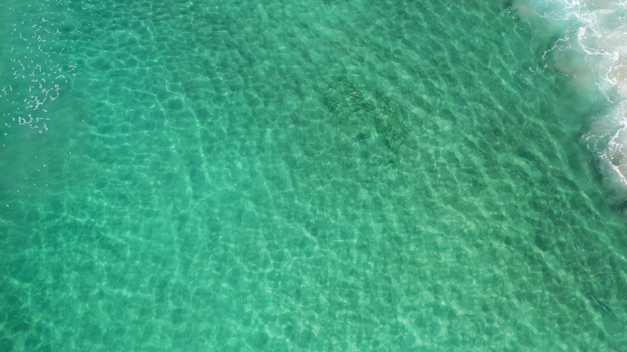 Top-down view of rippled teal sea with small surf entering from the right.