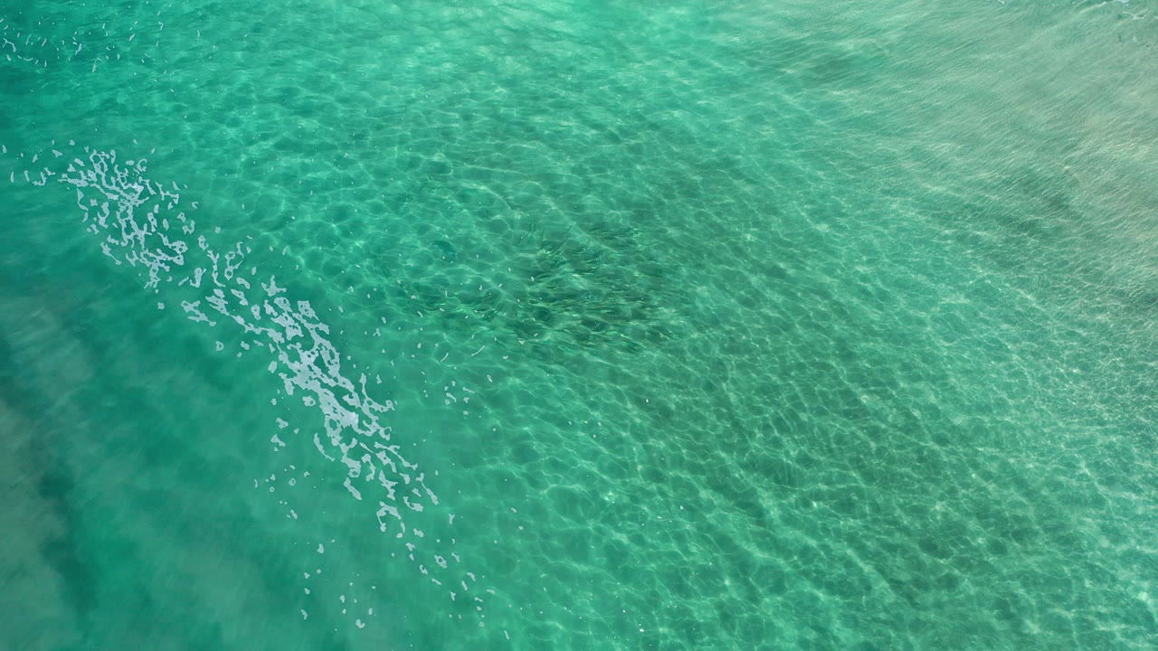 Overhead view of turquoise and deep green ocean water in Los Cabos, Mexico, with fine ripples, diagonal sun reflections, and no visible people.