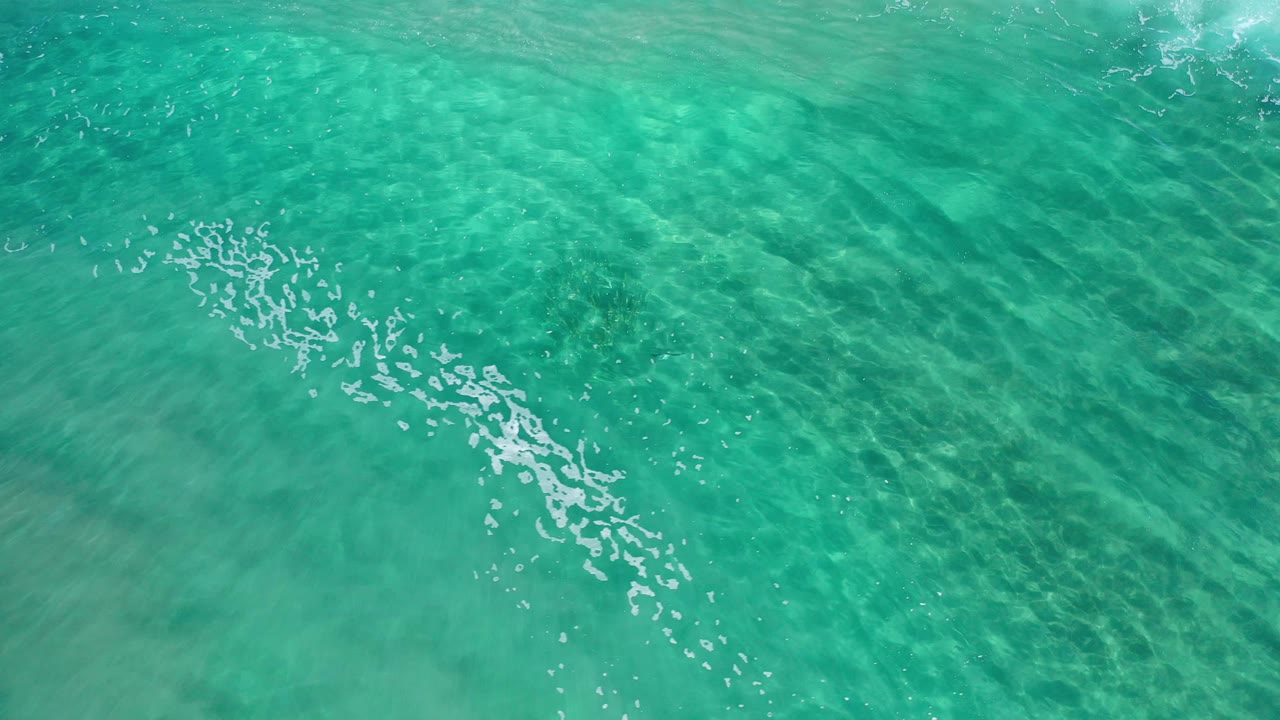 Bright turquoise shallow water with foam marks and darker patches below.