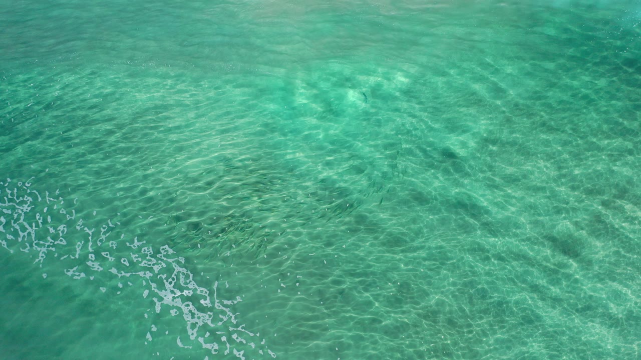 Clear turquoise ocean water with ripples and small foam flecks.