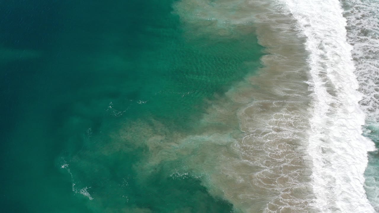Overhead turquoise water and white surf foam over sand.