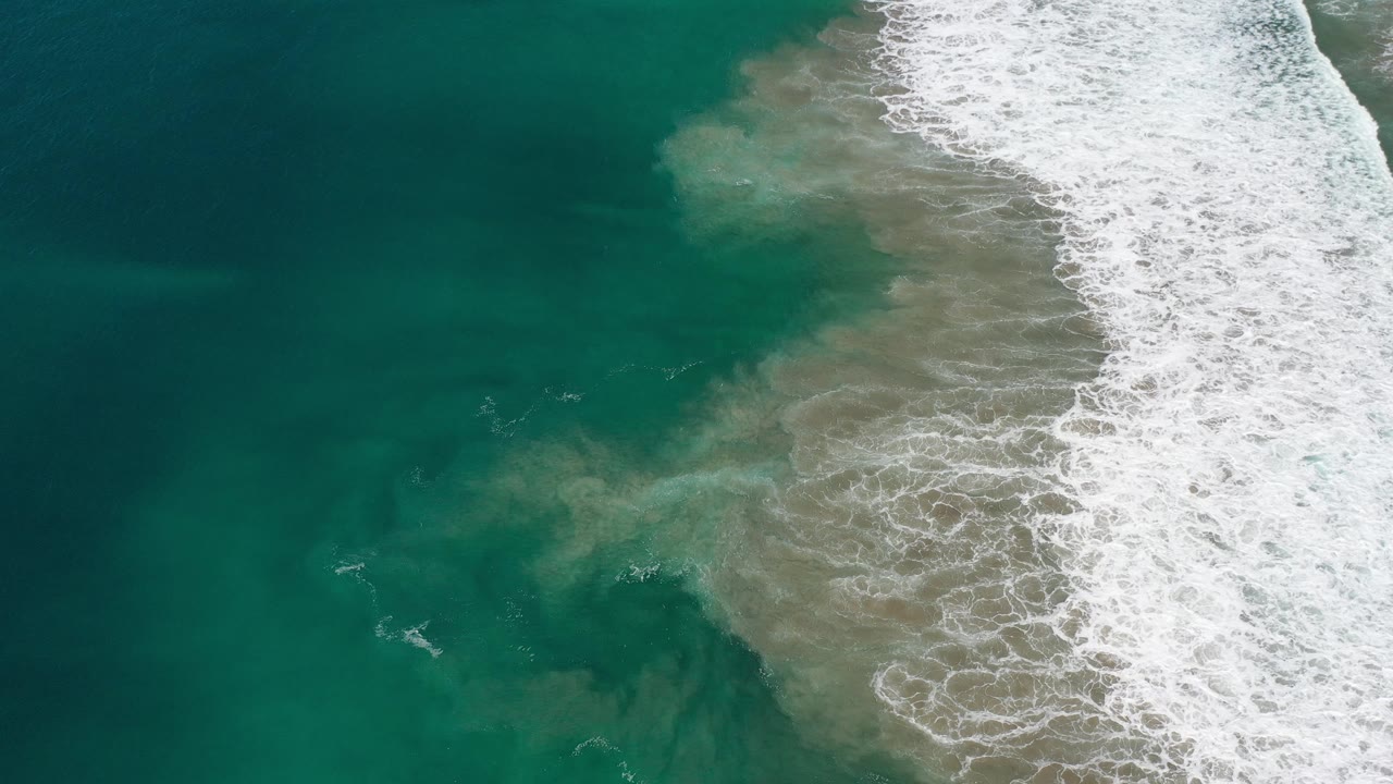 White wave break along a diagonal beach edge in green water.