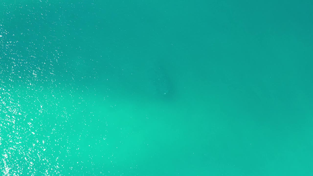 Los Cabos sea surface with a narrow vertical band of bright reflection near the center and no visible people.
