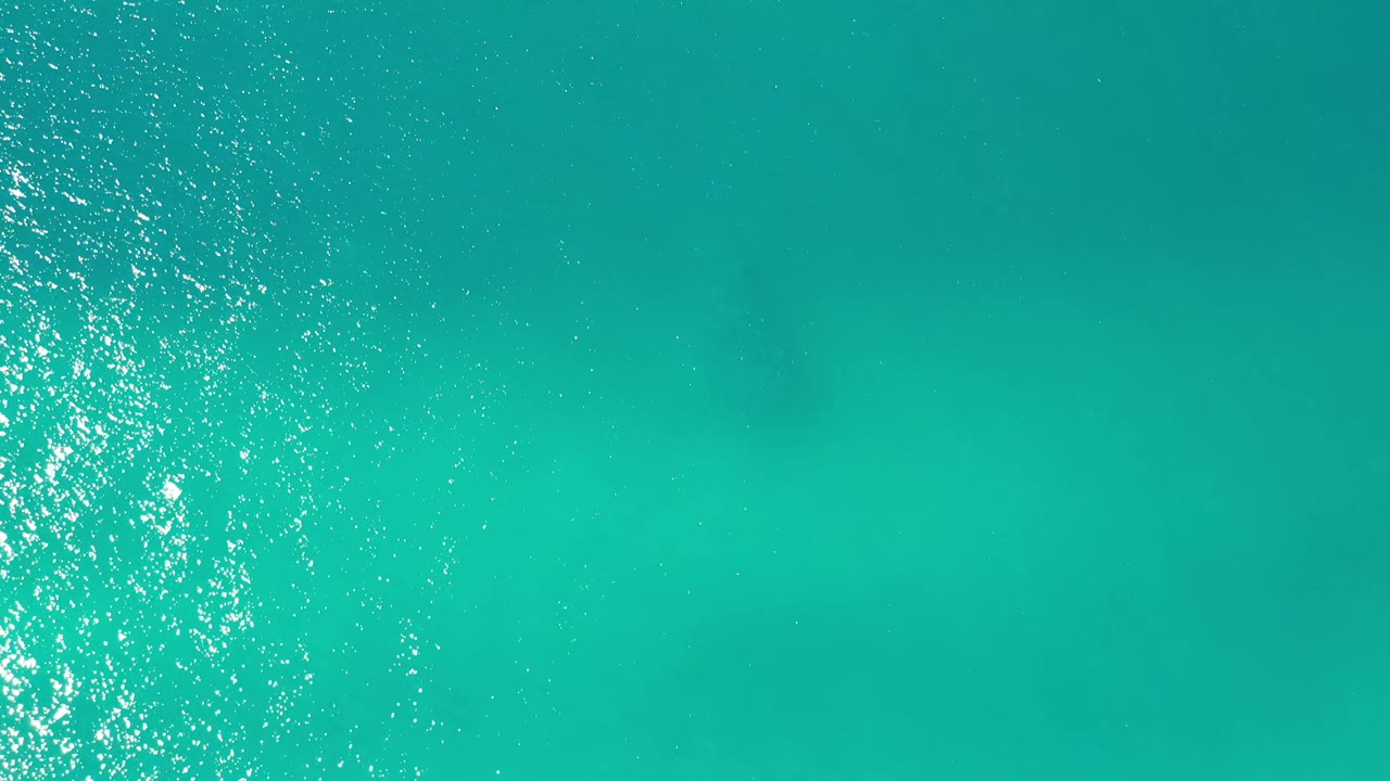 Aerial view of Los Cabos ocean water with a narrow bright reflection running down the frame and no visible people or boats.