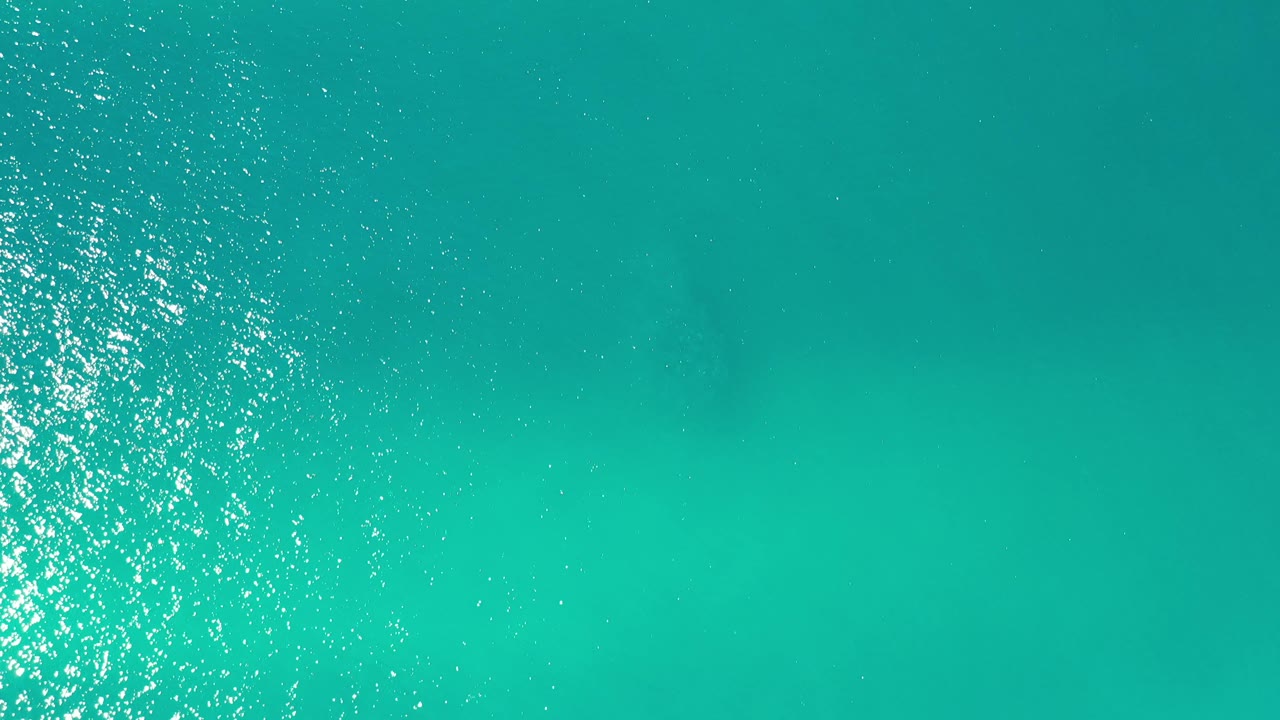 Turquoise sea surface with bright sparkle and faint darker patches.